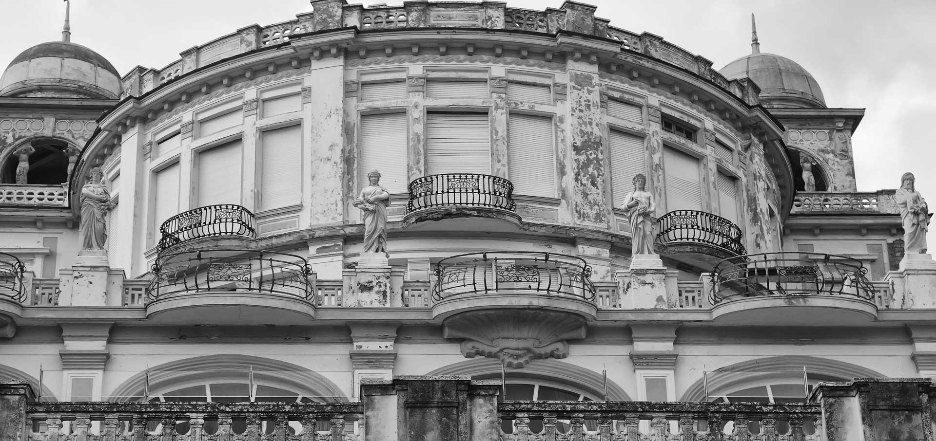 Black-and-white photo of a grand historic building with statues, curved balconies, and domed towers.