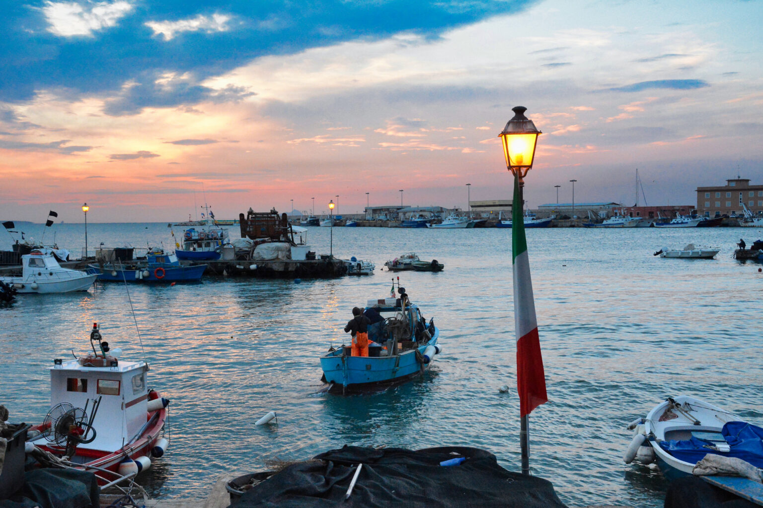Anzio Porto, peschereccio al tramonto con barche da pesca, pescatori su imbarcazione, lampione acceso e bandiera italiana sul molo