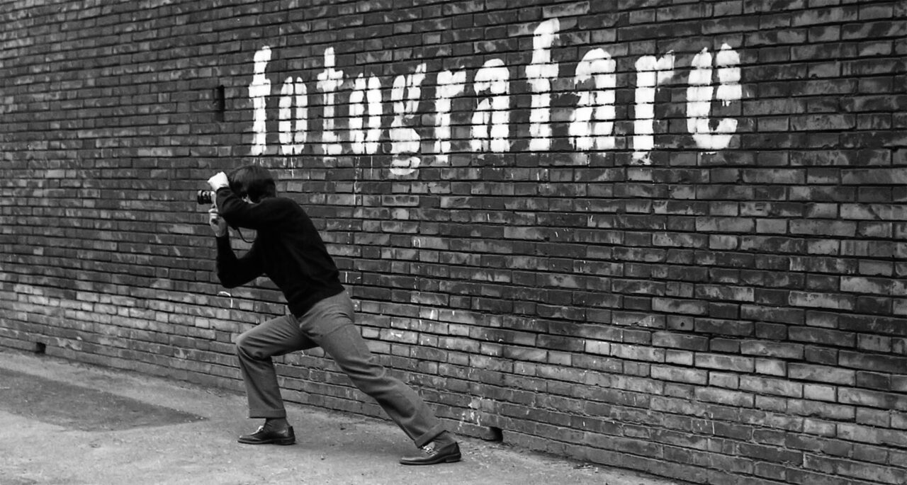 Crouching photographer with camera captures white graffiti on a brick wall; street art scene.