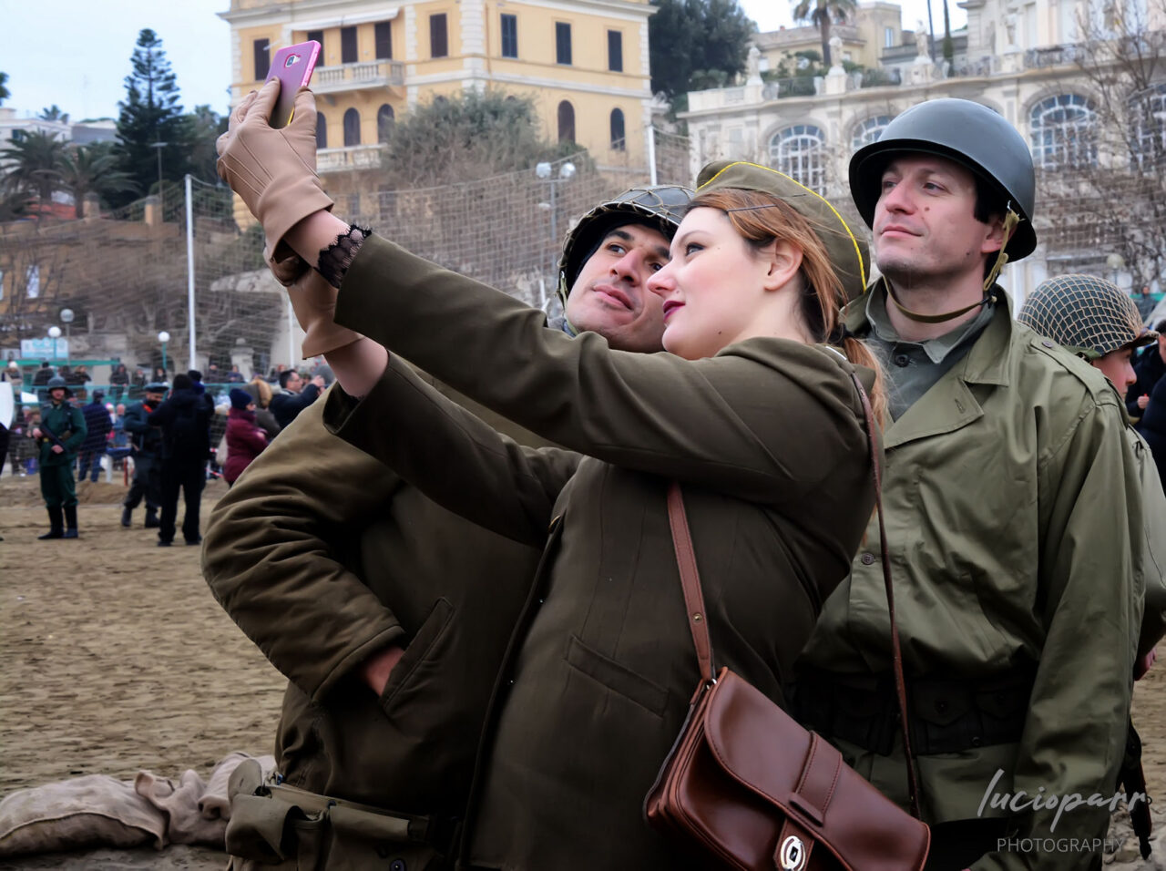 Woman and two men in vintage military uniforms taking a selfie at a historical reenactment.