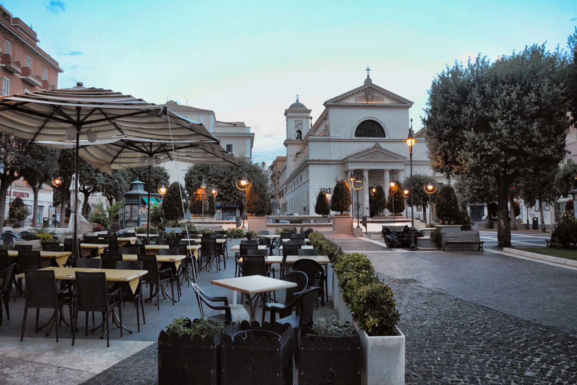 Outdoor cafe seating in a historic town square with a church, cobblestone pavements, and warm evening lights.