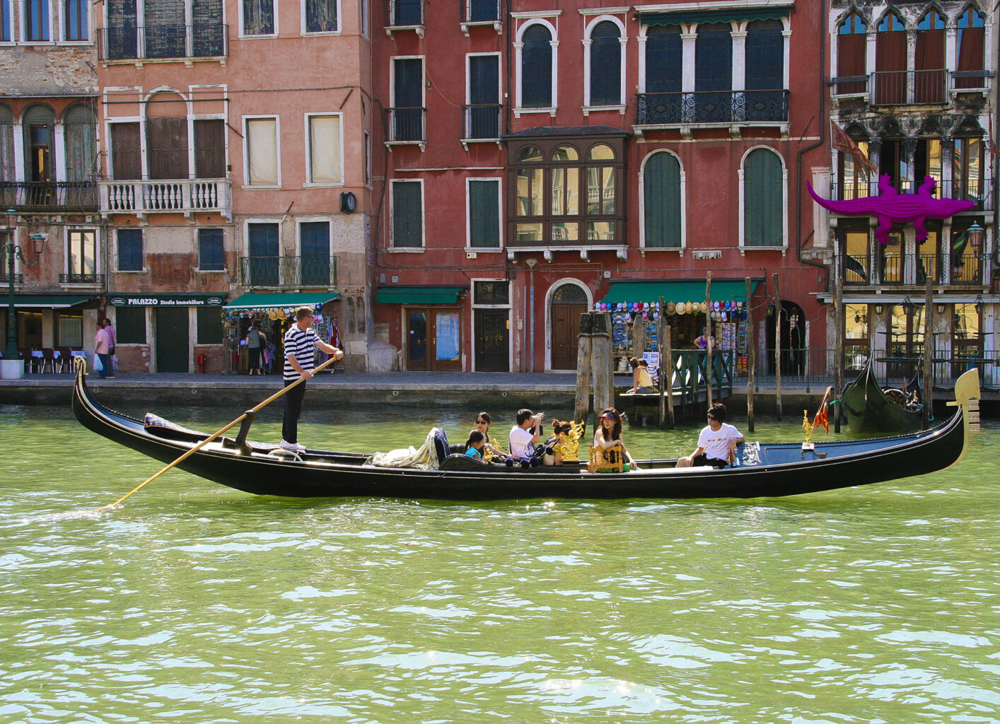 Gondola tradizionale con gondoliere e turisti sul Canal Grande a Venezia, palazzi storici e negozi sullo sfondo